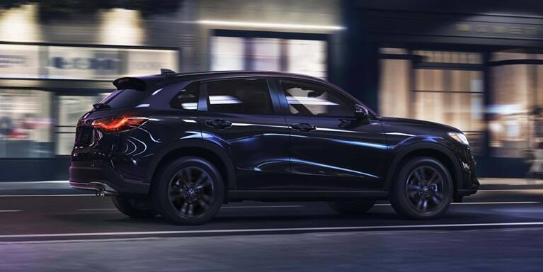 2027 Honda HR-V Sport in Crystal Black Pearl profile view driving through an urban street (Subcompact Crossover SUV).