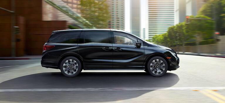 2027 Odyssey Elite family van in Crystal Black Pearl driving on a city street (Minivan).